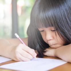 A girl writing at a table with her chin on her hand