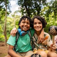Two kids in the woods smiling at the camera.